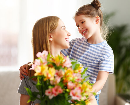 Girl hugging mother with bunch of flowers