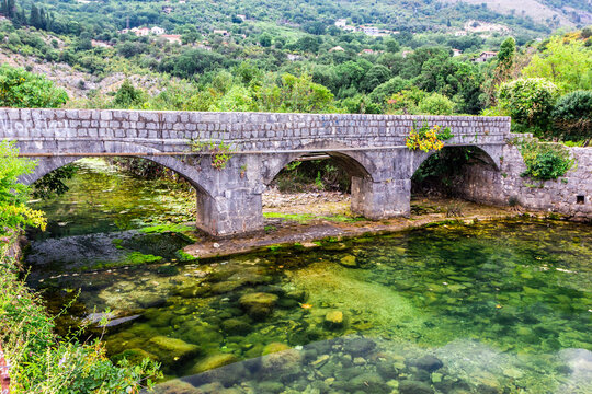 Old stone bridge over small transparent river at foot of mountains, near Risana, Boca-kotor bay, Montenegro