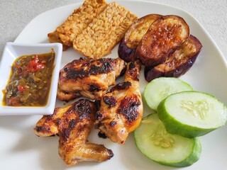 Ayam Bakar, Sambal, Tempeh, Eggplant and Cucumber on White Plate.