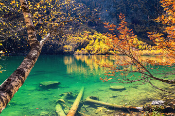 Beautiful landscape with mountain lake and high rocks with illuminated peaks reflection with green water, blue clean sky and yellow autumn sunrise.