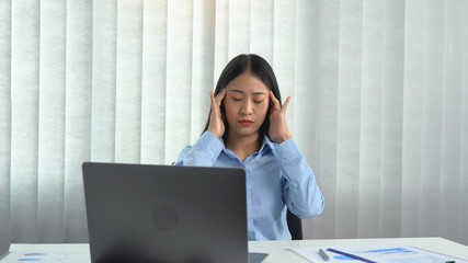 Asian woman sitting at work caused a headache so she gently rubbed her head with her hand.