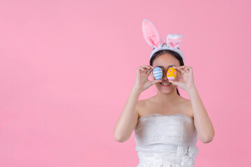smiling happy young woman wearing bunny ears and holding a of Easter eggs on pink background