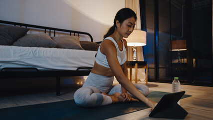 Young Asia lady in sportswear exercises doing work out and using tablet to watch yoga video...