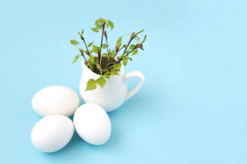 unpainted white easter eggs with green leaves on a branch