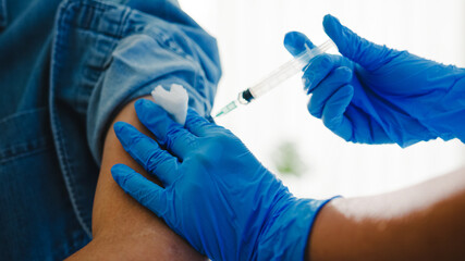 Young Asia lady nurse giving Covid-19 or flu antivirus vaccine shot to senior male patient wear face mask protection from virus disease at health clinic or hospital office. Vaccination concept.