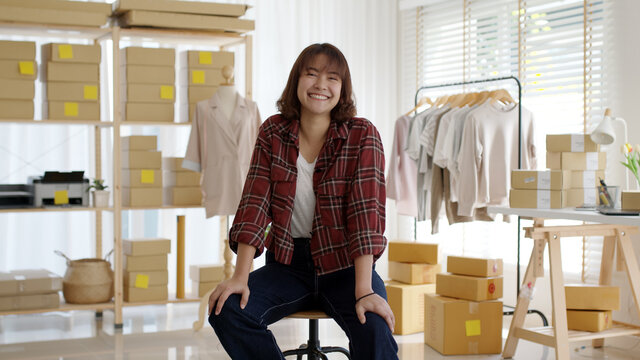 Portrait young attractive asia female owner startup business look at camera work happy with carton box at home prepare delivery in sme supply chain, procurement, omnichannel ecommerce online concept.