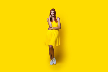 Monochrome photo of a caucasian woman with red hair in a yellow dress smiling at camera on studio wall