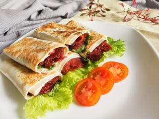 Kebab on White Plate. A delicious Kebab wrap with spicy meat, lettuce, tomato, and sauce. Selective Focus