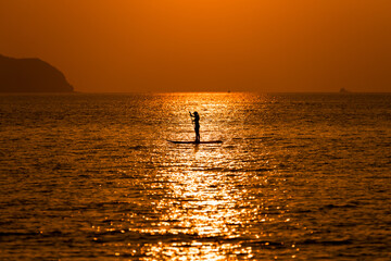 Silhouette sport girl stand up paddling on sup board or surfboard enjoy to play extreme sport on holidays at sunlight beach.