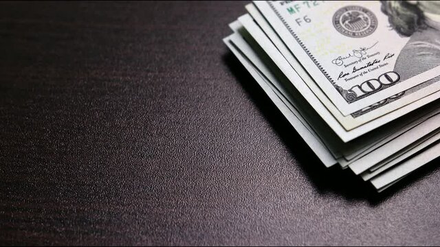 An increasing stack of one-hundred-dollar fiat money on a wooden surface. Space for the text. Concept of profit, successful investment. Stop-motion shooting