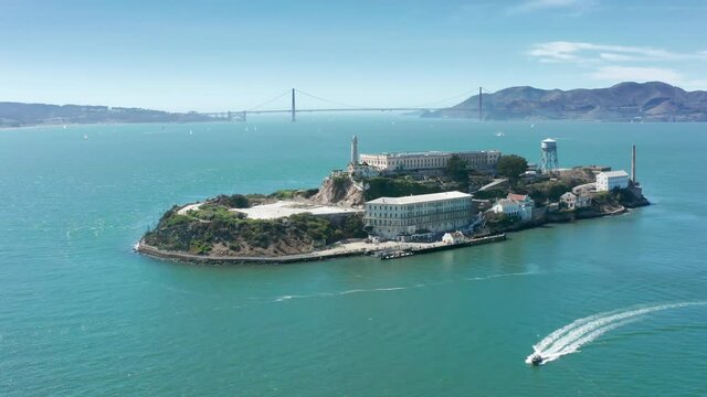 World famous touristic landmarks and attraction 4K. Aerial close up Alcatraz island with Golden Gate bridge on background. Historic prison building in green San Francisco bay area waters on summer day