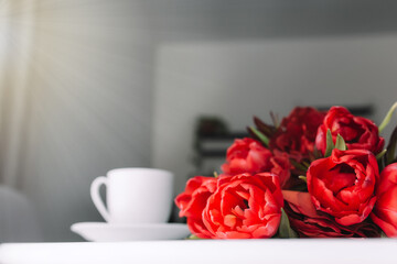 Bouquet of red tulips on table and white coffee cup. Concept for greeting card