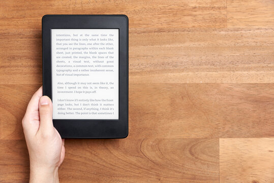 Young hand holding an electronic reader with text on the screen on a wooden desk