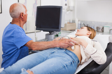 Mature male doctor using ultrasound scan examining female patient in modern hospital