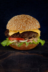 Juicy homemade burger on a wooden board against a dark background, shot close