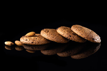 Oatmeal cookies with chocolate chips are isolated on a black background with a reflection. Lots of brown round homemade cookies lying on a reflective surface, close-up