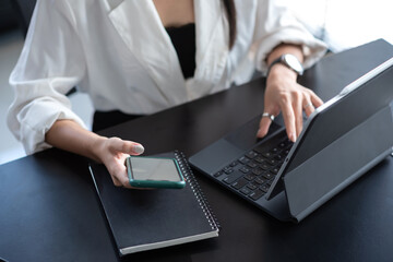 Close up of a woman hold mobile phone working on a keyboard tablet at the office.