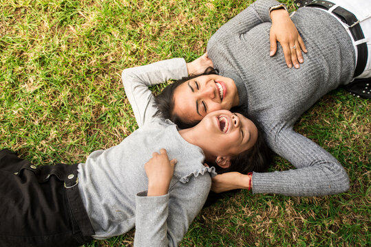 Laughing latin mother elder sister or young baby sitter playing outdoor on the grass with the little girl.