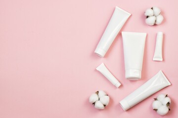 Natural spa cosmetics. White tubes on pink background with cotton flowers. Copy space. Flat lay. advertising. mockup.