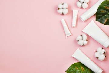 Natural spa cosmetics. White tubes on pink background with cotton flowers.green leaves. Copy space. Flat lay. advertising. mockup.