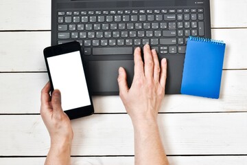 A female hand holding in a smartphone near a laptop on a wood white table. Close-up, top view. Planning concept, goal setting. Online shopping. Copy space. Flat lay.