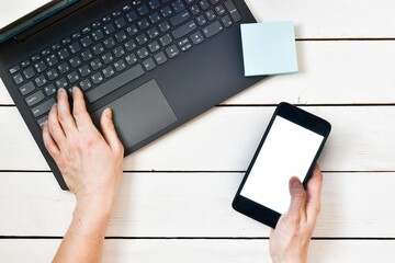 female hand holding in a smartphone near a laptop on a wood white table. Close-up, top view. Planning concept, goal setting. Online shopping. Copy space. Flat lay.
