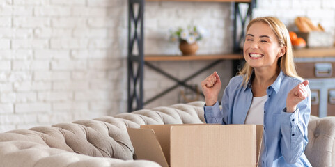 Happy young woman sitting on the couch and unpacking the long-awaited parcel