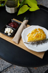 Scone, strawberry jam and cream on top in a white ceramic dish set on table.