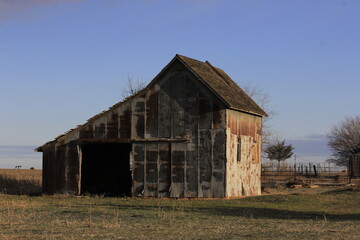 Obraz premium old abandoned barn with tree's, and blue sky in a Ghost town in Kansas.