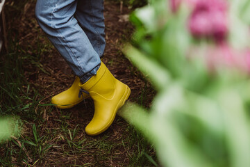 Unrecognizable woman gardener in yellow rubber boots. Soft selective focus.