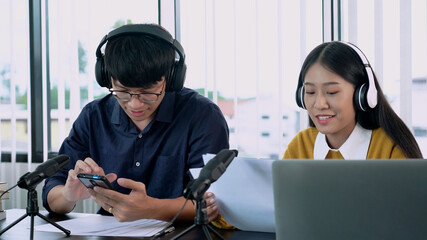 Asian woman radio hosts gesturing to microphone while interviewing a man guest in radio station during a show for radio live in the Studio.