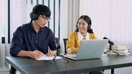 Asian woman radio hosts gesturing to microphone while interviewing a man guest in radio station during a show for radio live in the Studio.