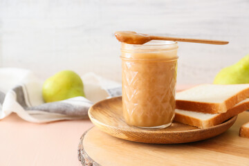 Jar of tasty pear jam with bread on wooden table