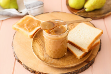 Jar of tasty pear jam with bread on wooden table