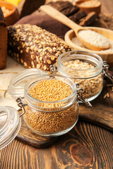 Jars with different cereals and bread on wooden background