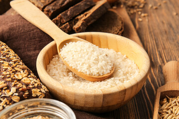 Bowl and spoon with rice on wooden background, closeup