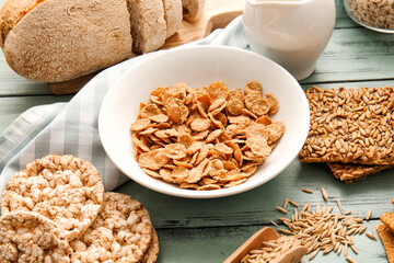 Bowl with cornflakes and different products on color wooden background, closeup