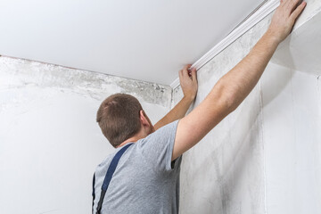 Worker fixes the plastic molding to the ceiling. Installation of ceiling cornice.