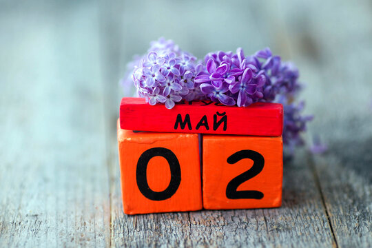 Wooden calendar with Russian text May 2 and a bouquet of lilacs on a wooden background. Copy space.