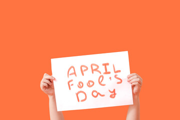Hands holding poster on color background. April Fools Day celebration