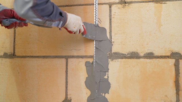 Installation of metal guiding beacons for filling and leveling of walls in the repair. Hand covers the wall with plaster. The worker fixes the metal beacons with mortar.