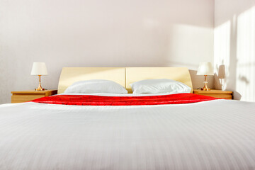 Fototapeta na wymiar Headboard of double bed in sunny bedroom with white sheets and two lamps on nightstands bedsides