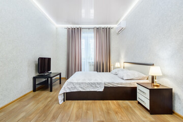 Simple interior of bedroom with double bed, tv, and two light-on lamps on nightstands....