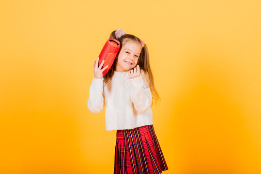 Young cute girl smiling and dancing with wireless portable speaker on yellow studio background.