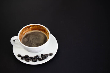White cup of aromatic coffee on a black background. The cup is on the saucer. White cup of aromatic freshly ground arabica coffee on a black background. Top view. with copy space.