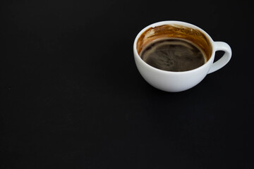 White cup of aromatic coffee on a black background. The cup is on the saucer. White cup of aromatic freshly ground arabica coffee on a black background. Top view. with copy space.
