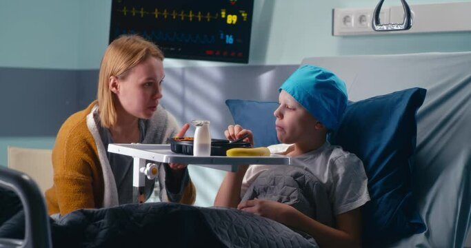 Mother talking with eating son in hospital ward