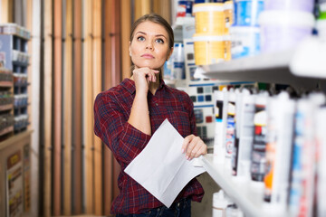 Perplexed woman designer is choosing paint with list for redecorate house in household shop