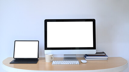 Front view of computer and digital tablet with blank screen on wooden office desk.