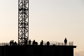Silhouettes of workers on construction site against the sky. Housing construction, builders working on scaffolding